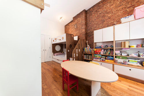 Cozy children's playroom with a brick wall, shelving full of toys, and a wooden dollhouse.