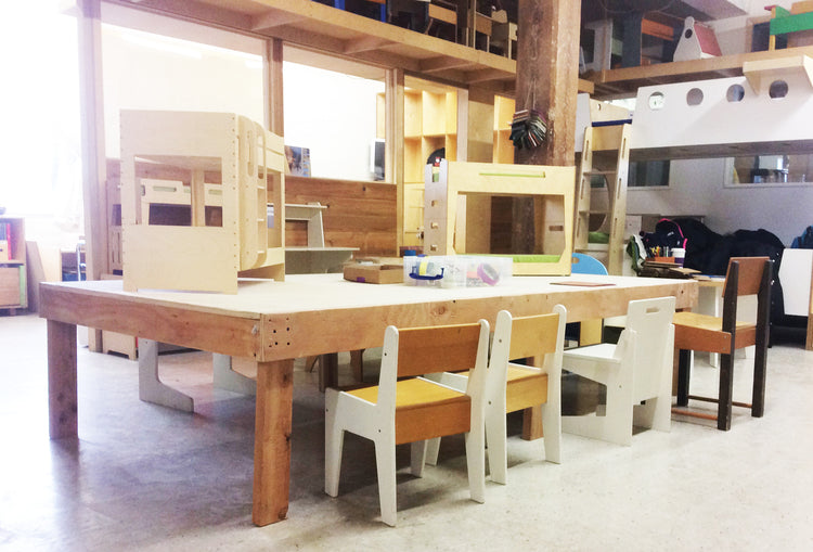 Large wooden table with chairs and dollhouses in a spacious children's play area.