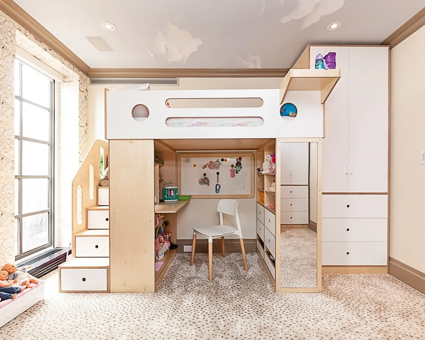 Child’s bedroom with loft bed, desk, storage stairs, and spotty rug.
