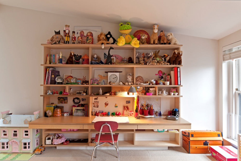 A room with a large shelf full of toys and books, a desk with a chair, and toys on the floor.