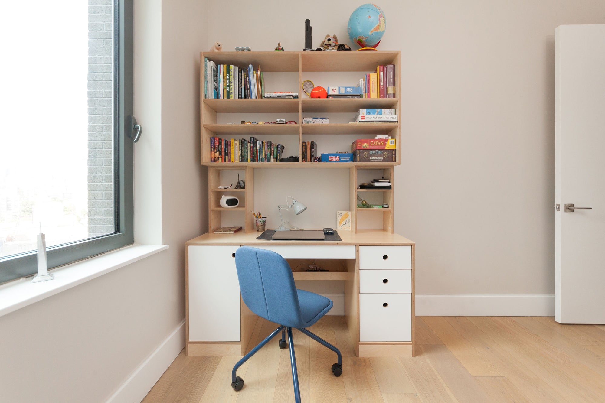 Modern study area with a wooden desk, shelves filled with books, a blue chair, and bright natural light.
