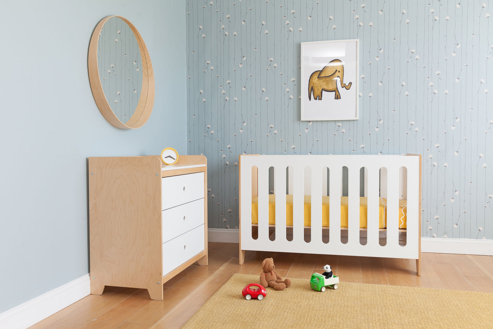 A modern baby's room with a crib, dresser, and toys on a rug, under an elephant picture