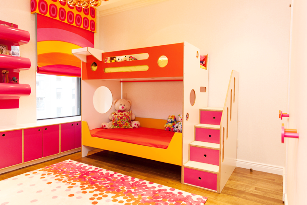 Colorful children’s room with a bunk bed, pink walls, and a patterned rug.