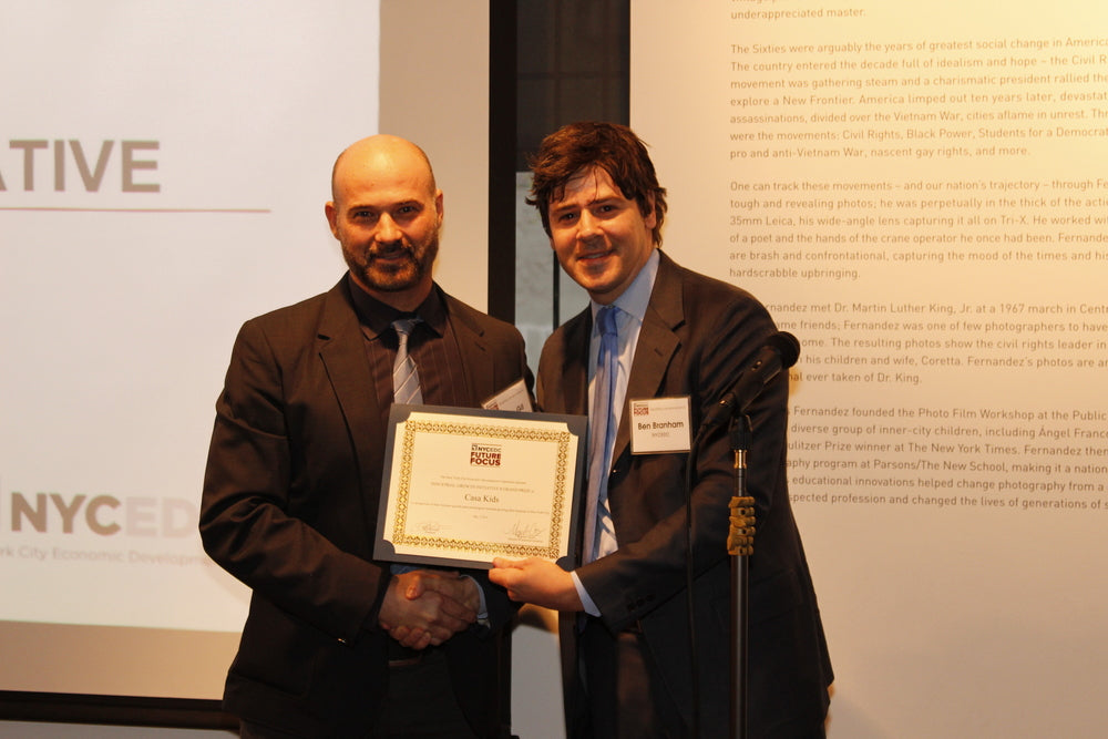 Two individuals with obscured faces holding a certificate in front of a presentation screen.