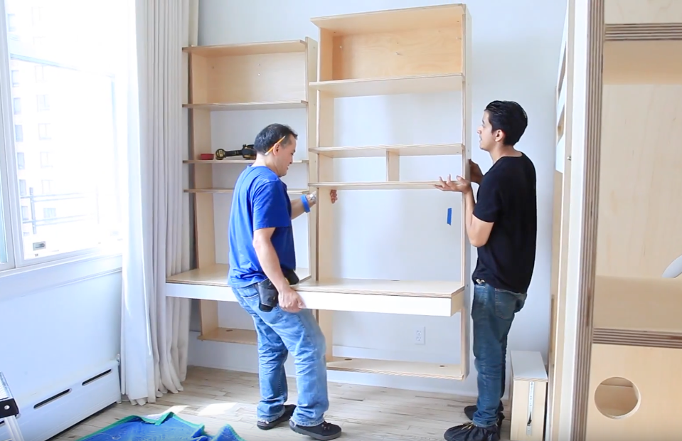 Two people assembling furniture in a bright room, one holding a shelf.