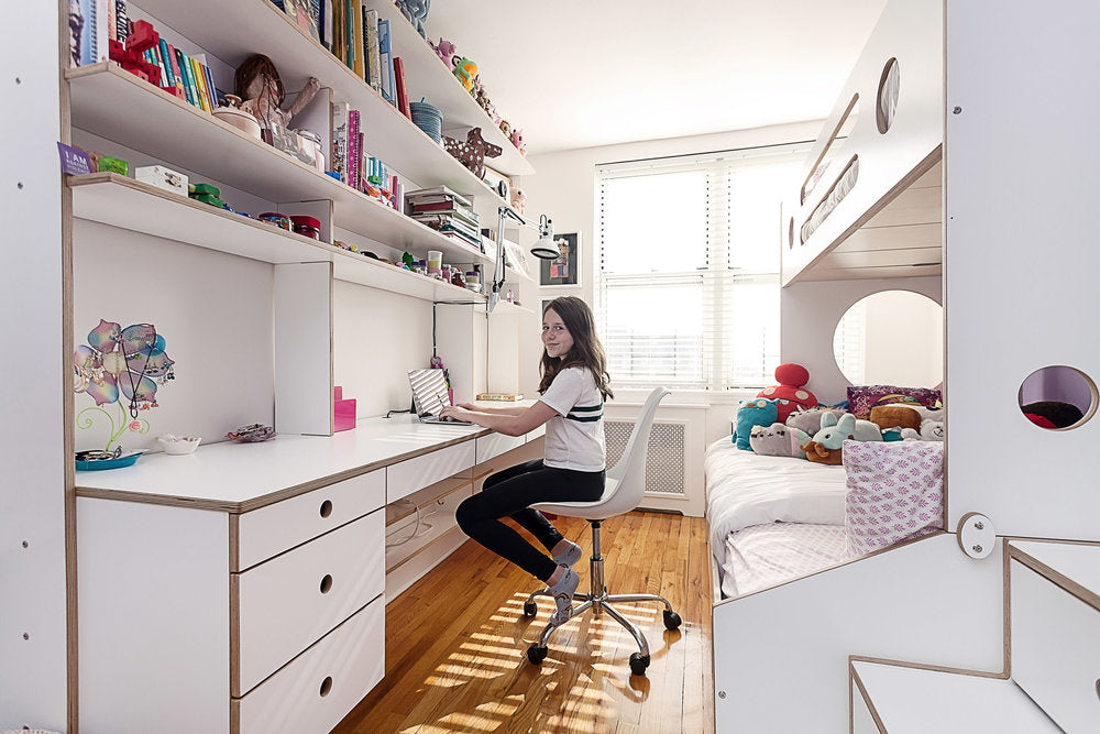 Bright workspace with white desk, shelves, decor, and seated person.
