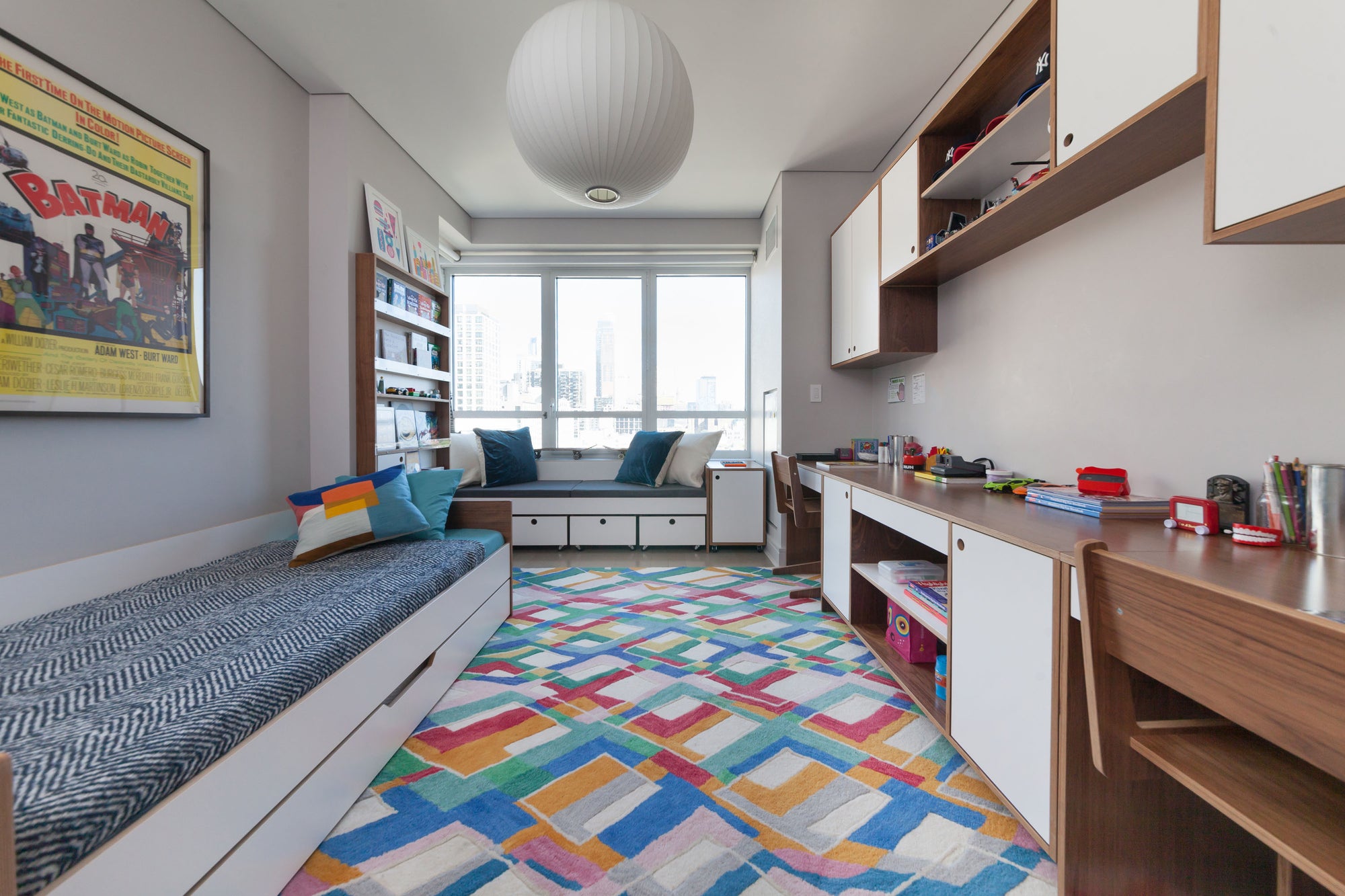 Bright child's room with bed, study desk, colorful rug, and window seating area.