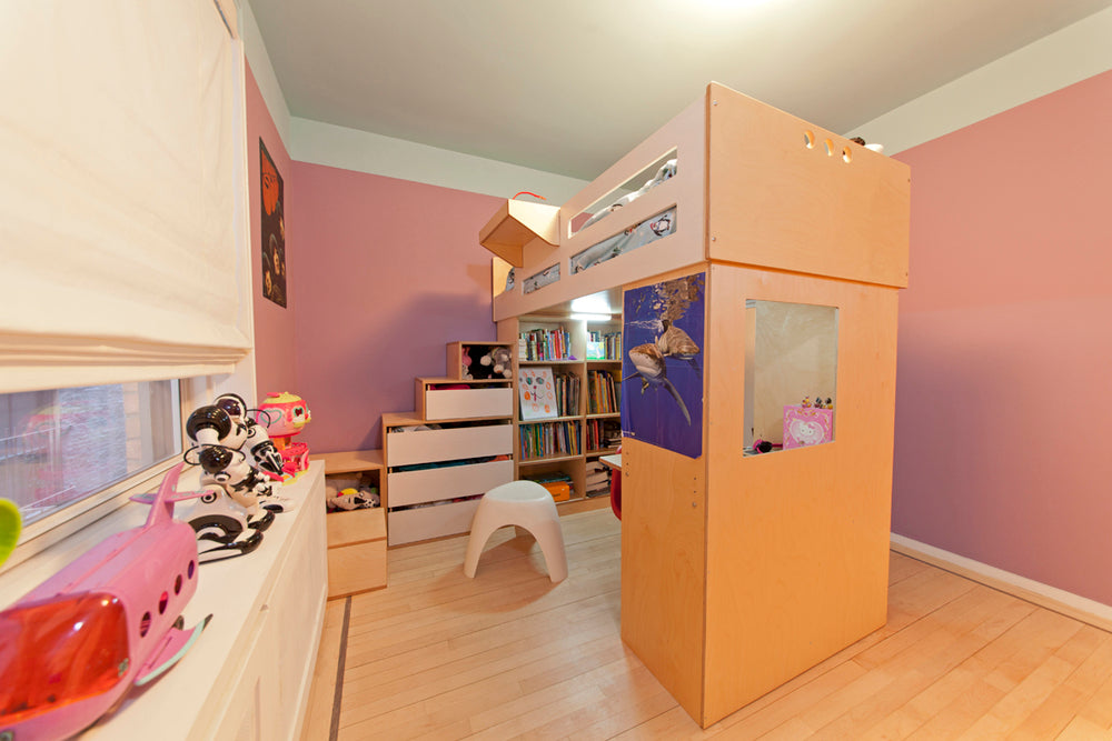 A cozy pink-walled child’s room with a loft bed, desk, toys, and books.