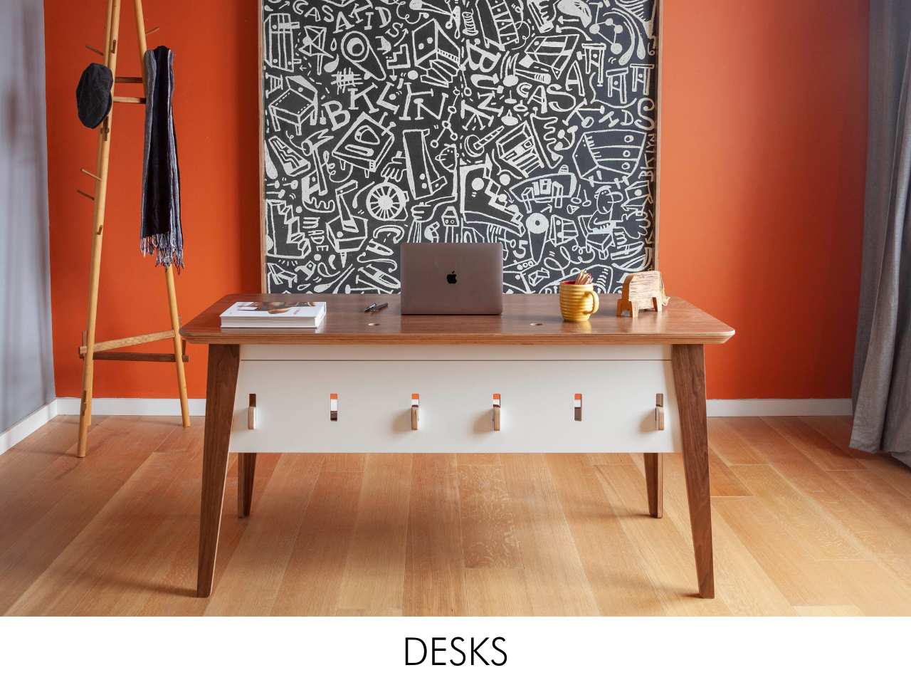 Stylish workspace with a wooden desk, laptop, vivid orange wall, and a detailed black and white mural.
