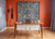 Modern home office with an abstract art piece, wooden desk, and coat rack against a vibrant orange and gray wall.