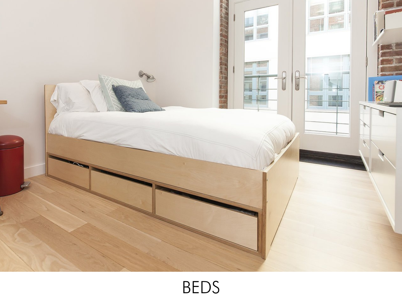 Modern minimalist bedroom with a wooden platform bed, white bedding, and hardwood floor.