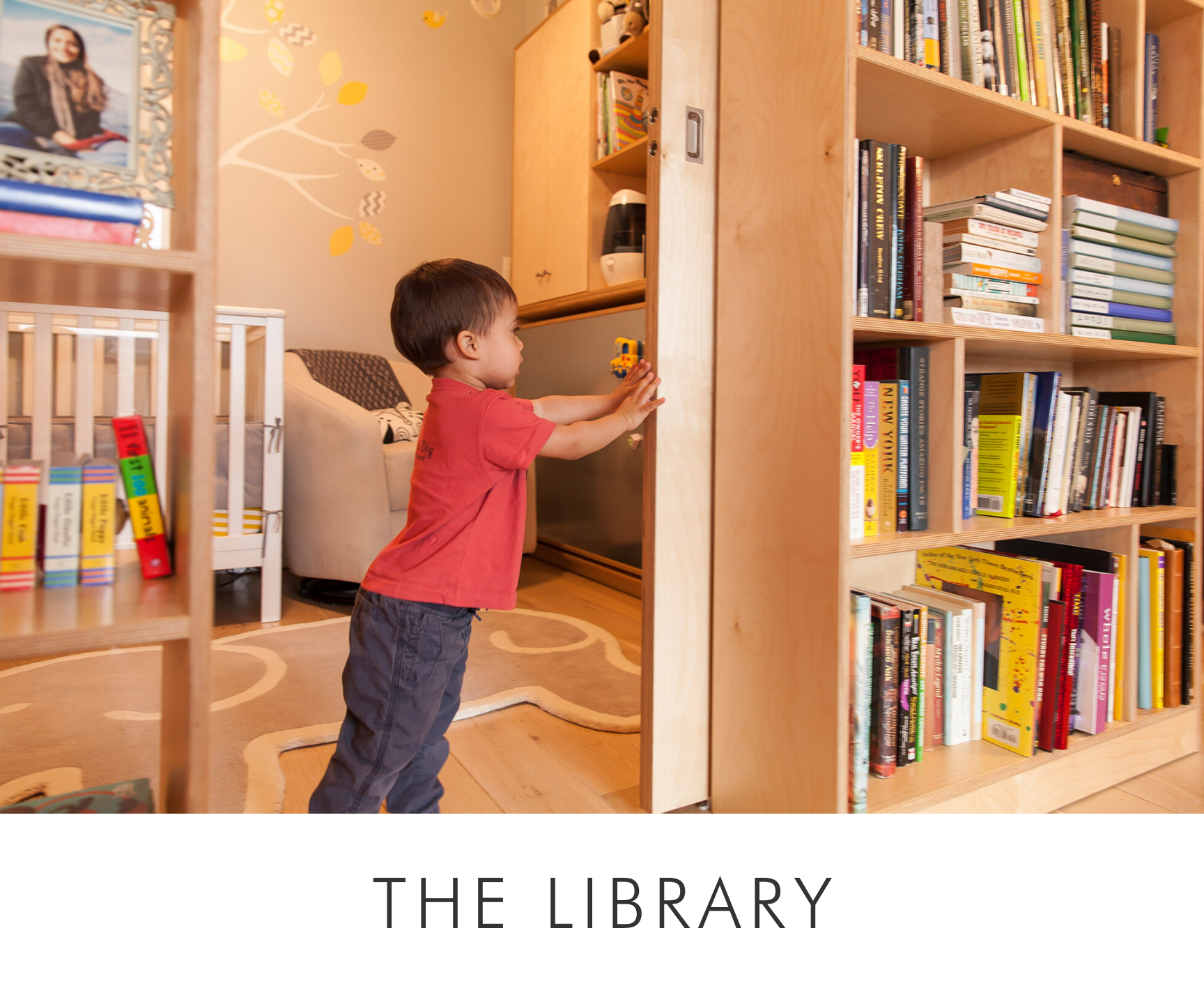 Young child reaching for a book in a cozy library with wooden shelves and a playful rug.