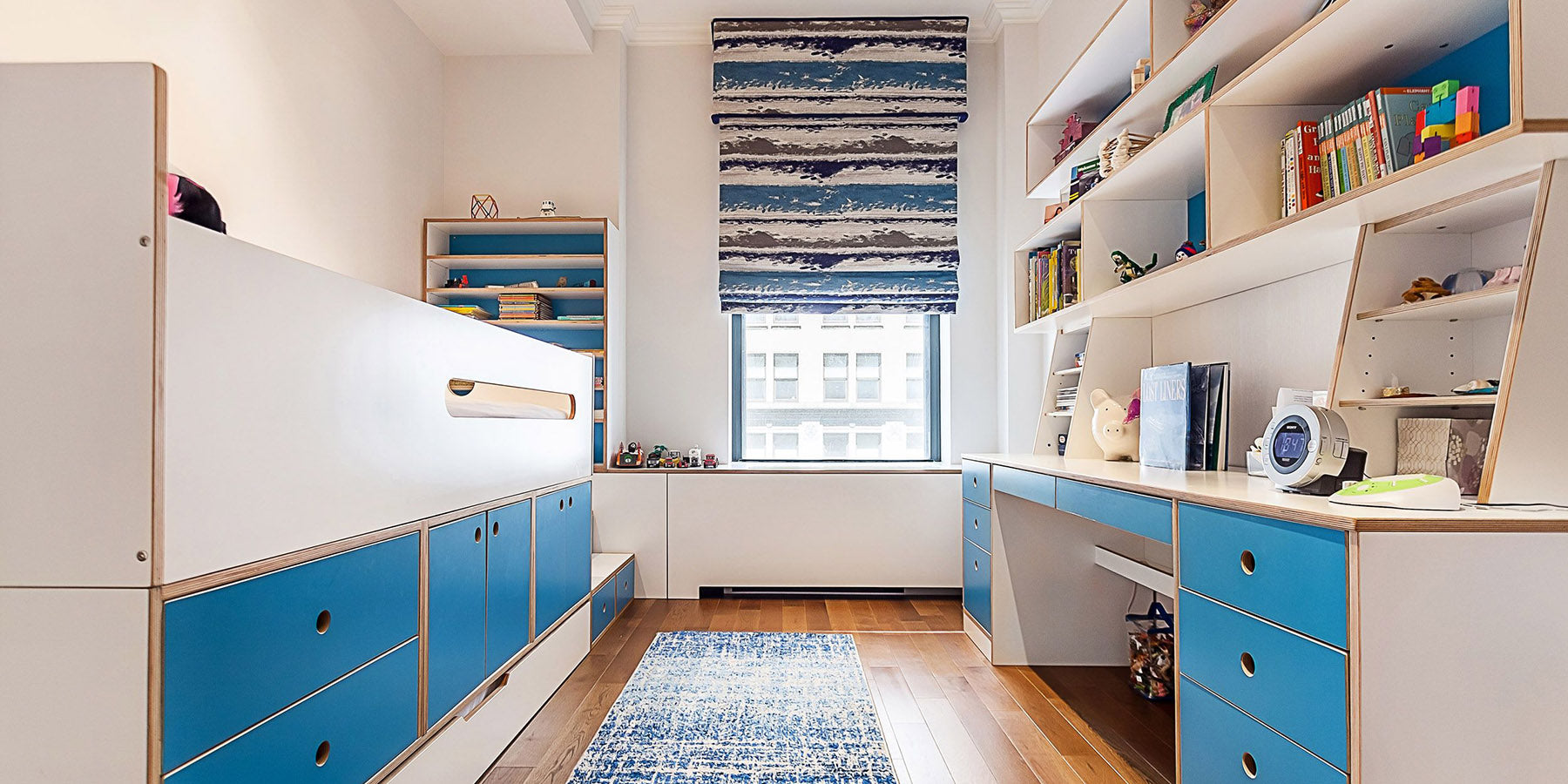 Modern child's room with white and blue storage units, built-in shelving, and a cozy study area.