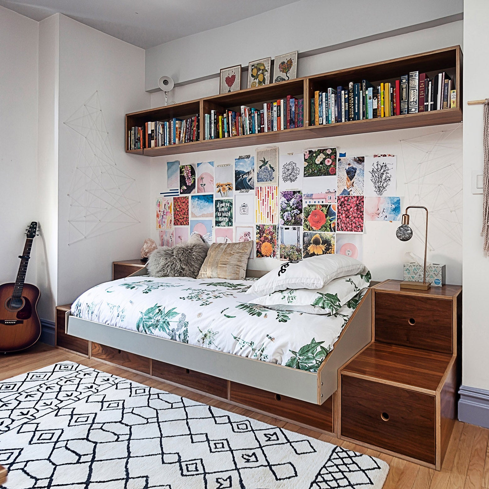 Cozy bedroom with a full-size bed, botanical bedding, wall filled with art and books, and a geometric rug.