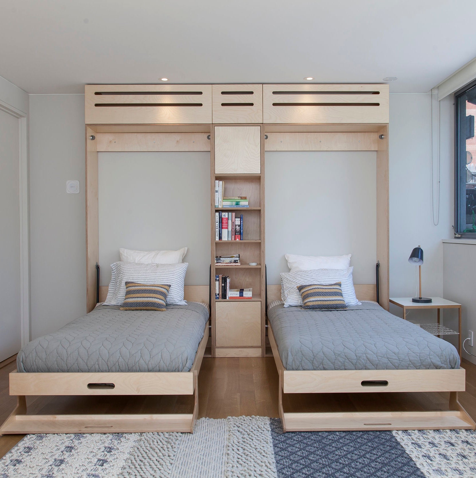 Modern minimalist bedroom with two twin beds that slide under a shared shelving unit, stylish and practical.