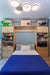 A tidy bedroom with a double bed, blue bedspread, built-in shelving, toy storage boxes, and a modern ceiling light fixture.