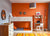 A vibrant kids' room with an orange accent wall, a bunk bed with doodle designs, a wooden dresser, and a small study area.