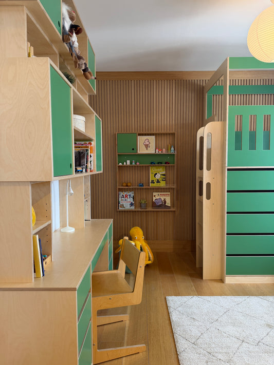 A children's bedroom featuring a light wood and mint green modular furniture set, including a desk, chair, bookshelves, storage cabinets, and a loft bed frame, with a slatted wood accent wall behind.