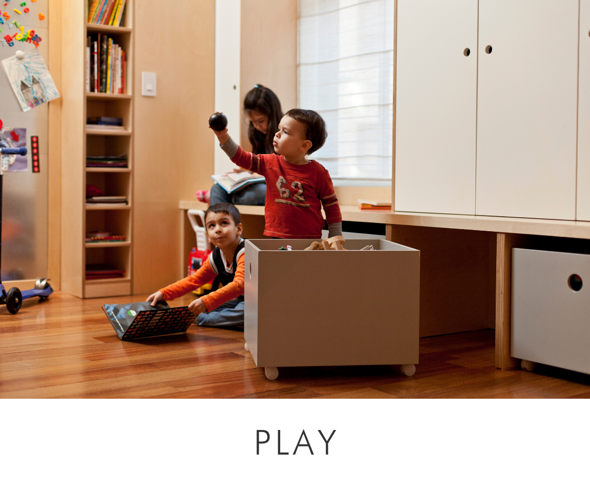 Children playing in a room with wooden floors, large cabinets, and a toy storage box.