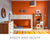 Vibrant room with an orange wall, patterned bunk bed, striped rug, and a desk with chair.