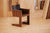 Dark wooden chair with a sleek design and a black seat, set against a plywood background.
