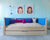 A colorful kids' room with a blue daybed, purple and pink pillows, light blue walls, and two framed artworks above the bed.