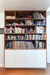 Modern wooden bookcase filled with assorted books and albums, featuring white storage cabinets below.