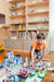 A child playing with a toy city setup on the floor in a room with built-in shelves filled with books and toys.