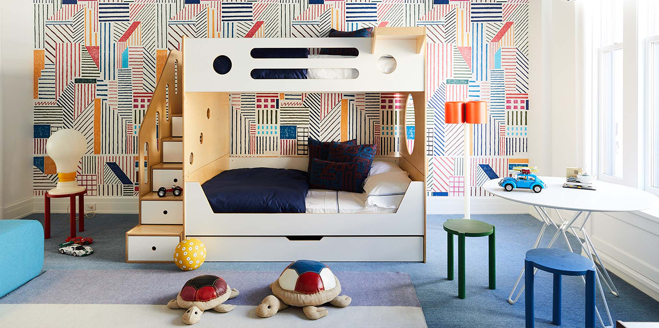 Modern children's room with geometric wallpaper, white bunk bed, and playful seating areas.