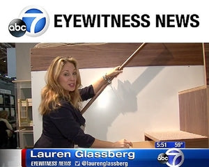 News reporter demonstrating features of a multifunctional furniture piece on a TV segment.