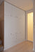 Sleek white built-in wardrobe in a minimalist corridor with wooden flooring and a softly lit room adjacent.