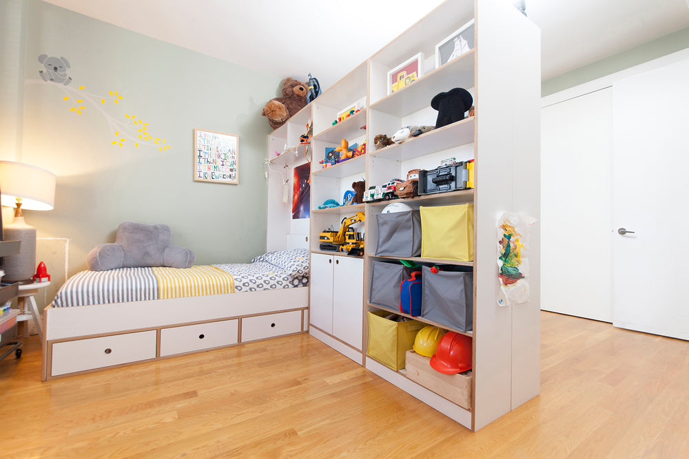 Bright and neat child's bedroom with bed and shelving full of toys and books.