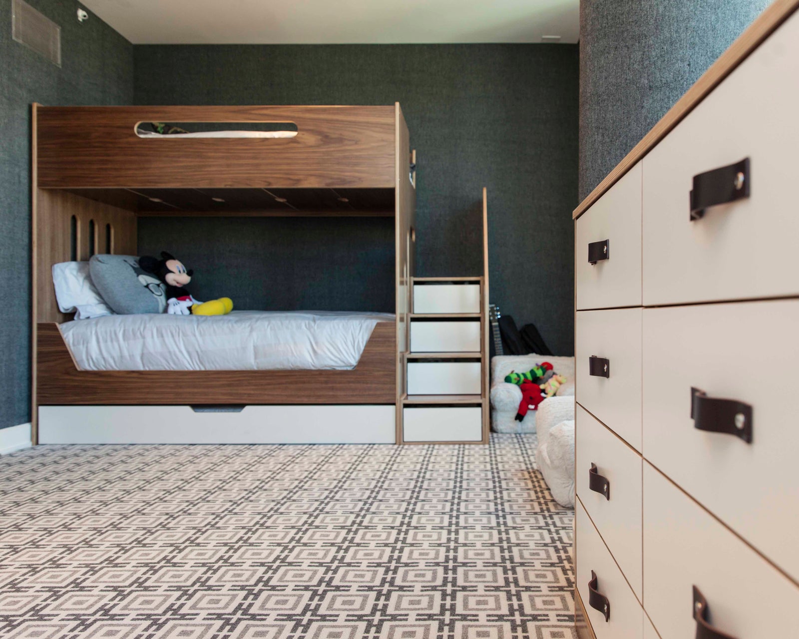 Children’s bedroom with bunk bed, storage cabinet, ladder, toys, and patterned carpet.