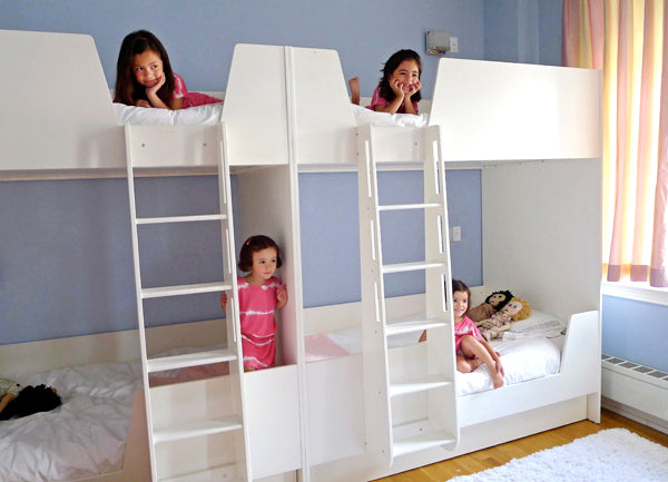 Four children playing on white bunk beds in a bright blue bedroom, having fun.