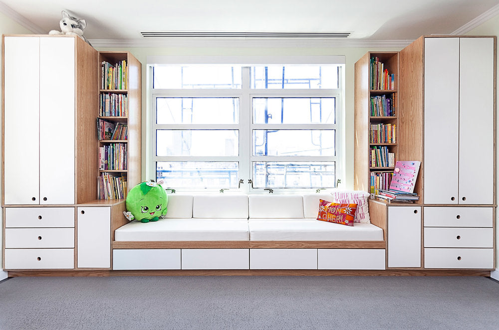 Bright room with a cozy window seat, bookshelves, and cabinets, inviting relaxation.