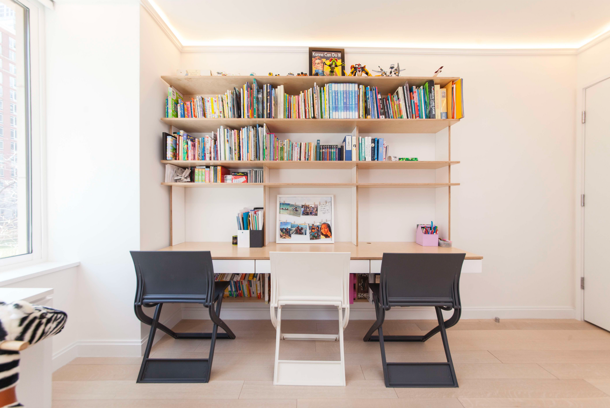Modern study area with a white desk, two chairs, and a large bookshelf filled with colorful books.