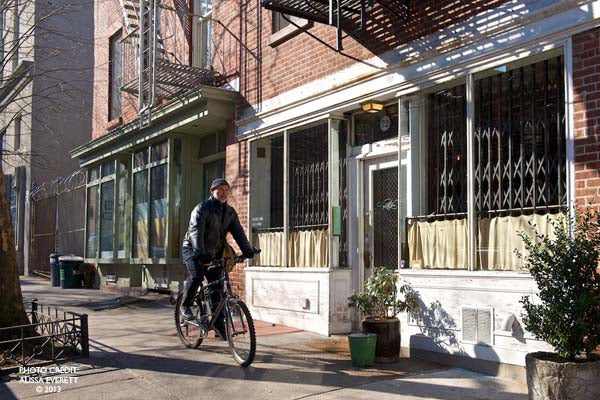 Cyclist riding in city beside brick buildings under clear skies.