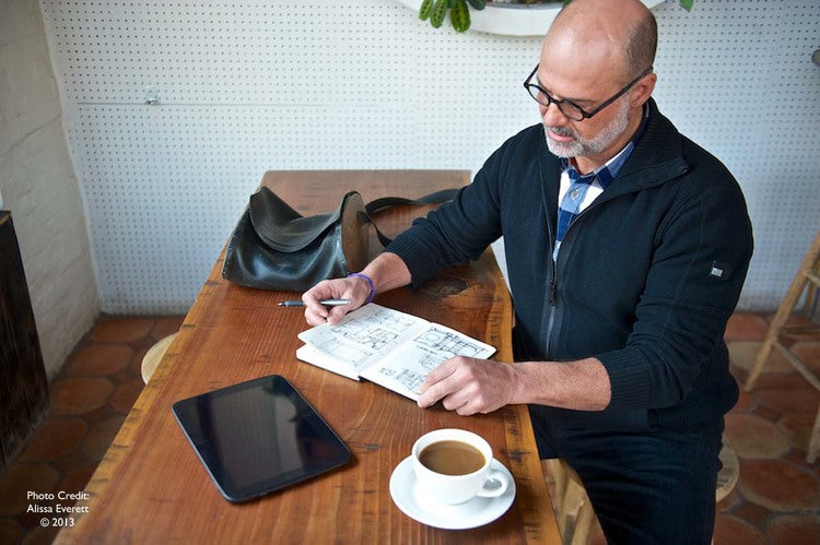 Person at table with newspaper, coffee, and tablet.