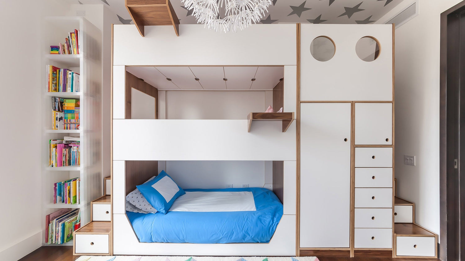 White and birch bunk bed in navy room with dark wood floor, blue rug, and grey bedding with white wall frames