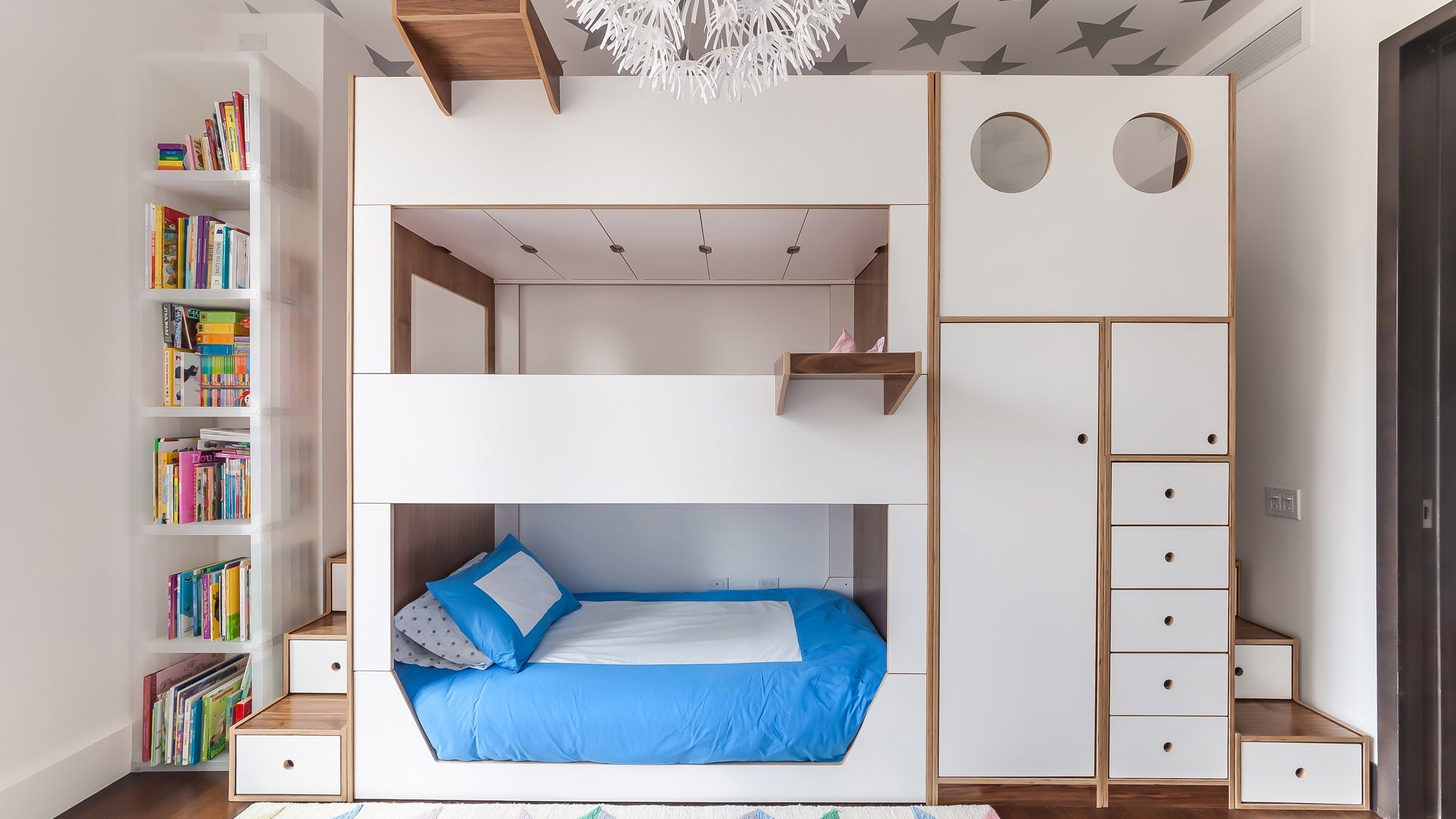 White and birch bunk bed in navy room with dark wood floor, blue rug, and grey bedding with white wall frames