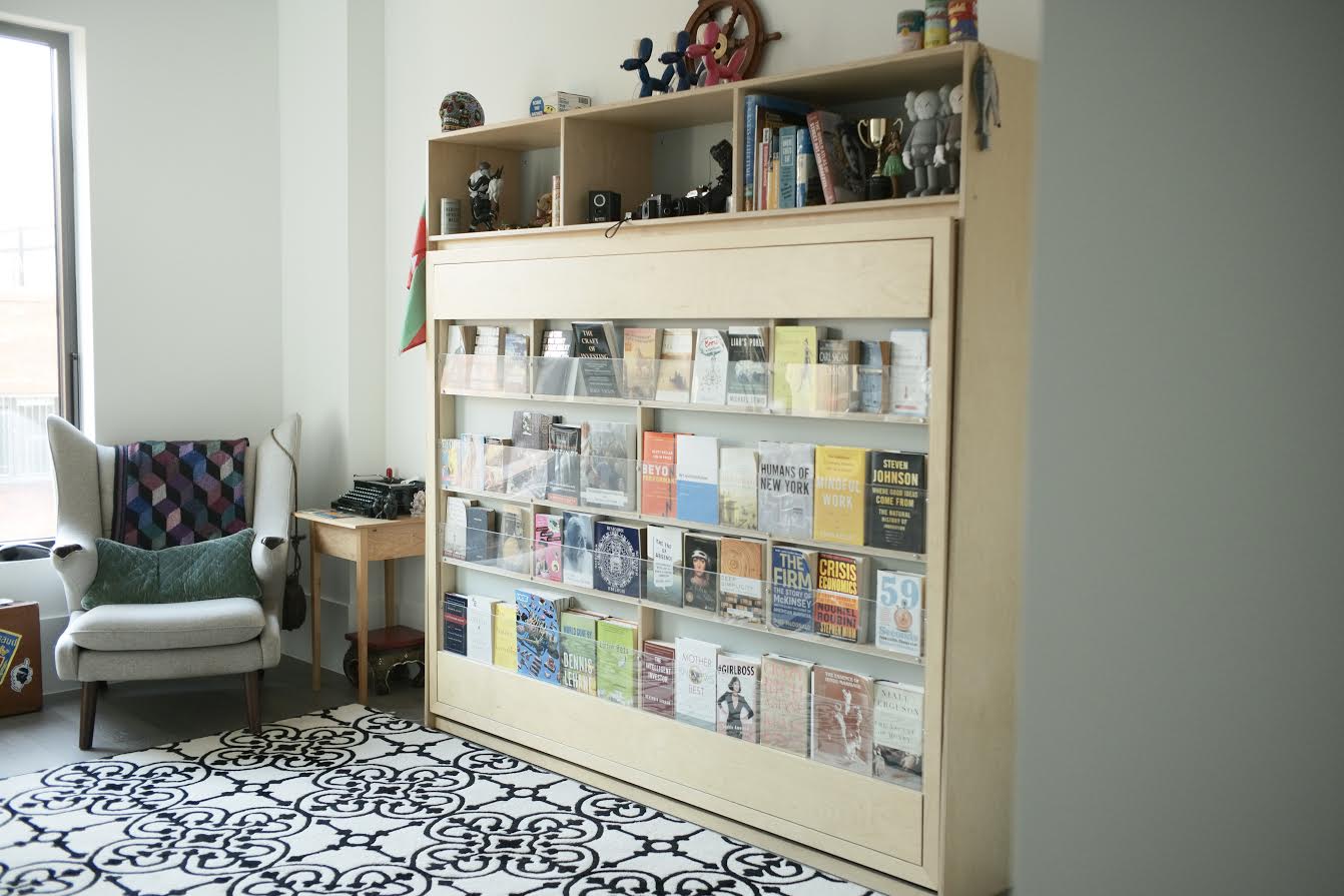 Spacious living room featuring a large bookshelf filled with books and magazines, next to a cozy chair.