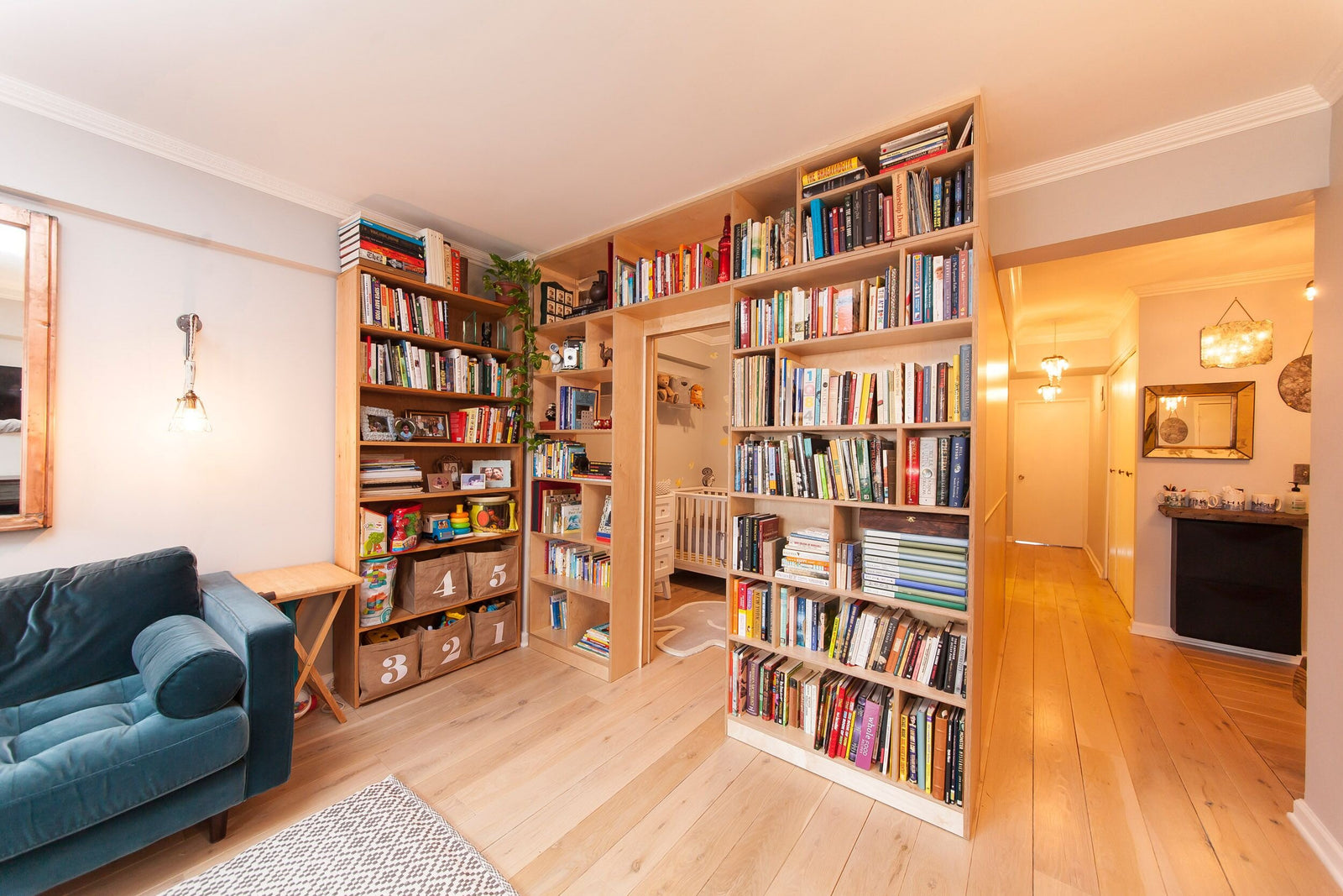Cozy living room with floor-to-ceiling bookshelves full of books, a blue sofa, and warm wooden flooring.