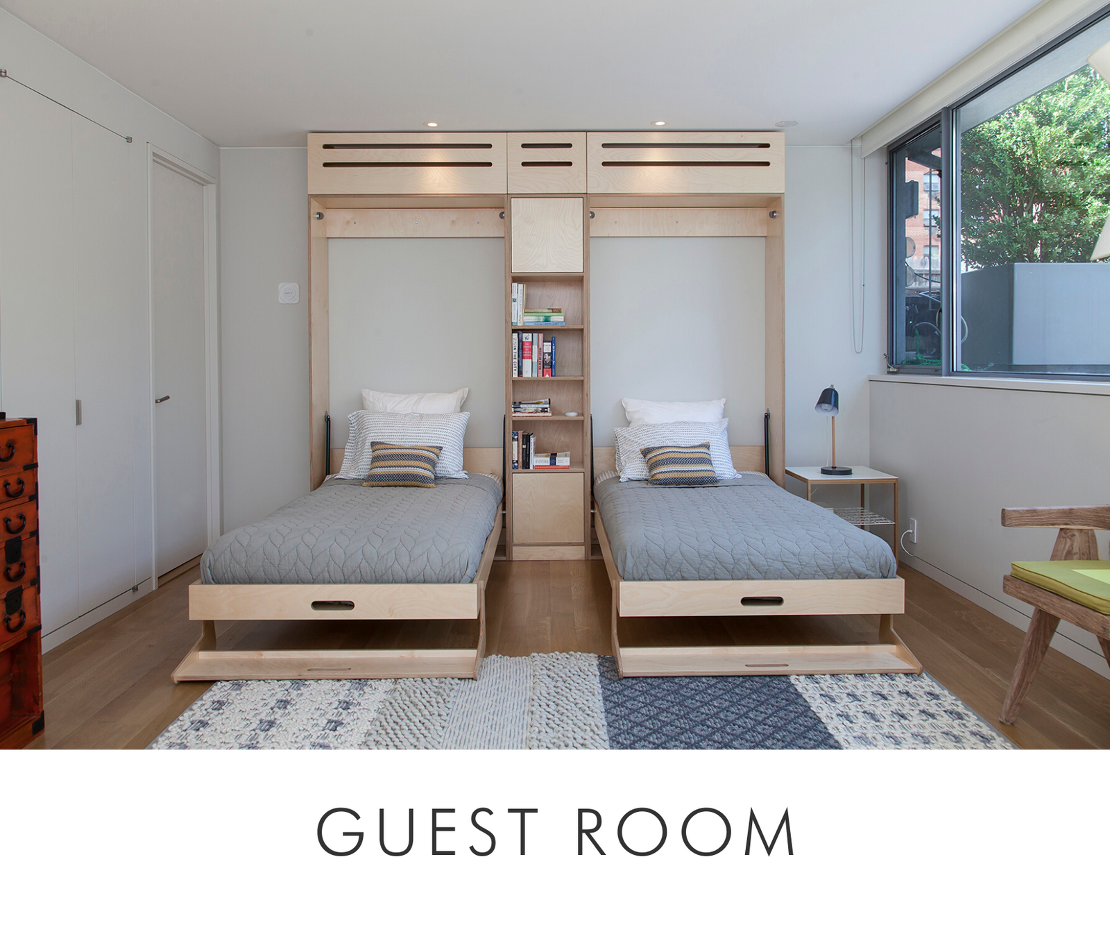 Modern guest room with two twin beds, built-in storage, large window, and a patterned area rug.