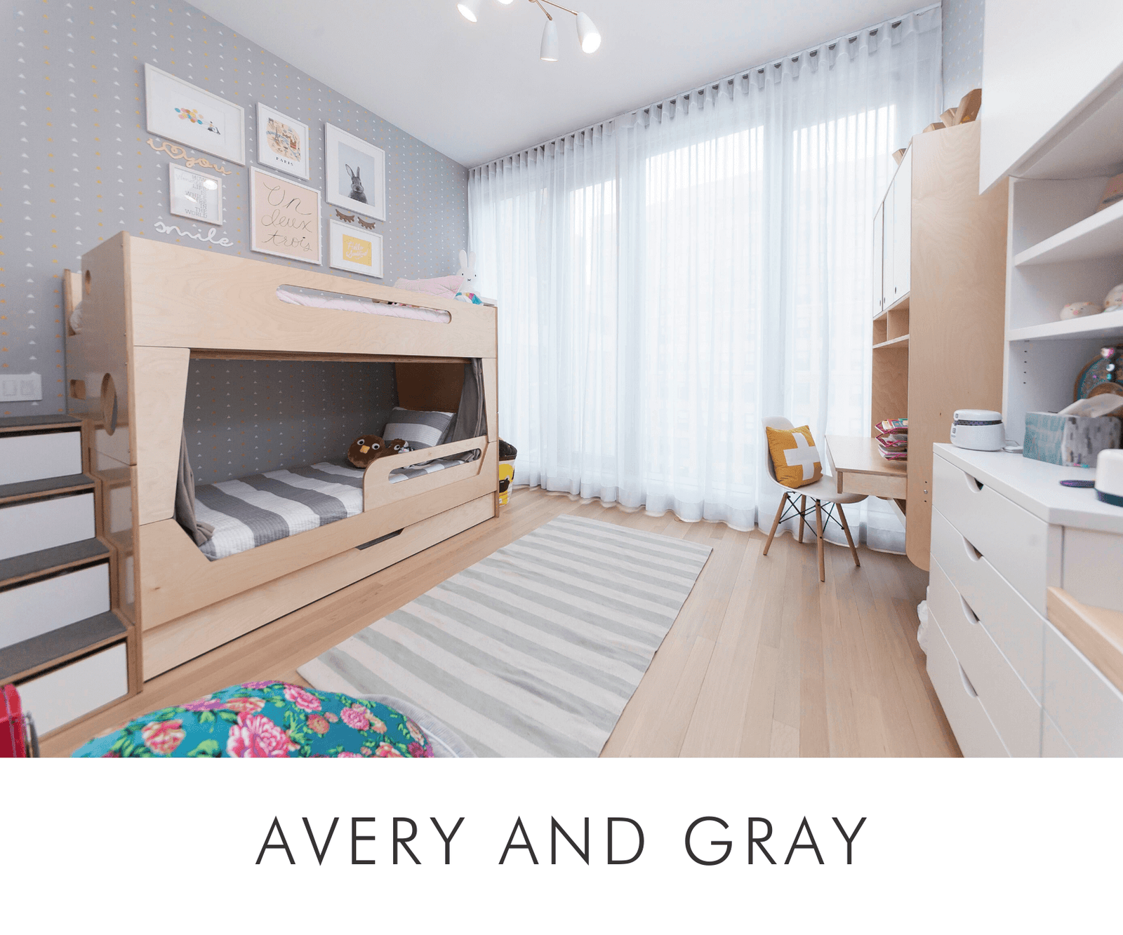 Light-filled room with bunk beds, desk, striped rug, and large window covered with sheer curtains.