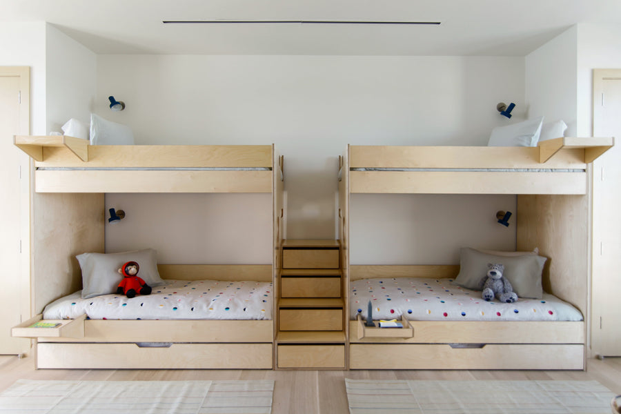Two sets of bunk beds with a central staircase, each bed neatly made with dotted bedding and adorned with a plush toy.