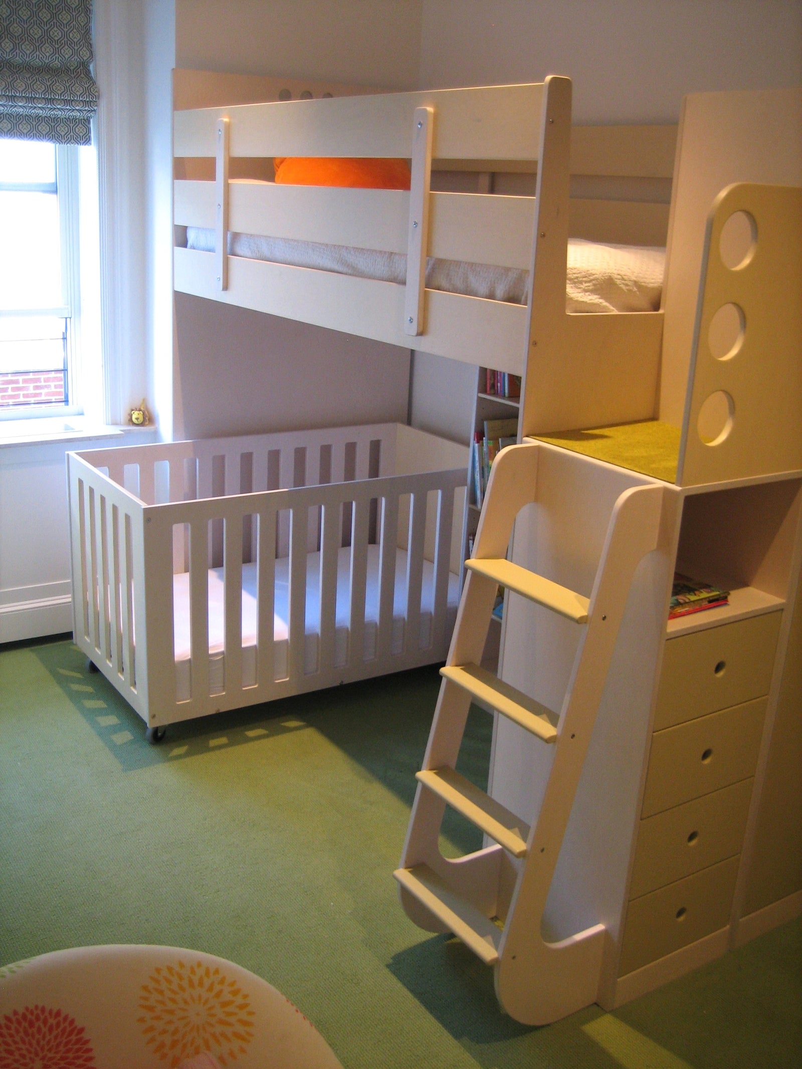 Bedroom with a white bunk bed, ladder, crib underneath, green carpet, and a window with patterned curtains.