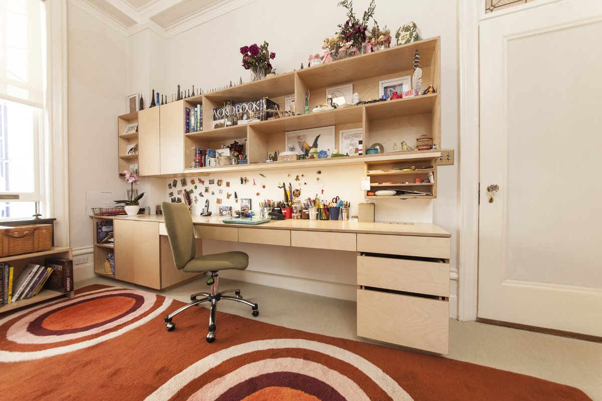 Warm home office with built-in wooden shelves, a desk, ergonomic chair, and colorful circular rugs.