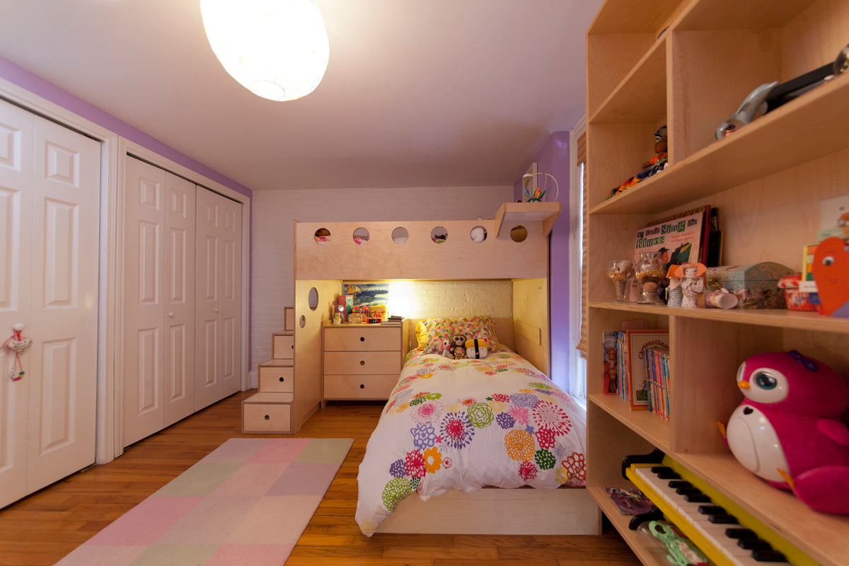 A cozy children's room with a loft bed, colorful bedding, storage stairs, a built-in bookshelf, and a soft pastel rug.