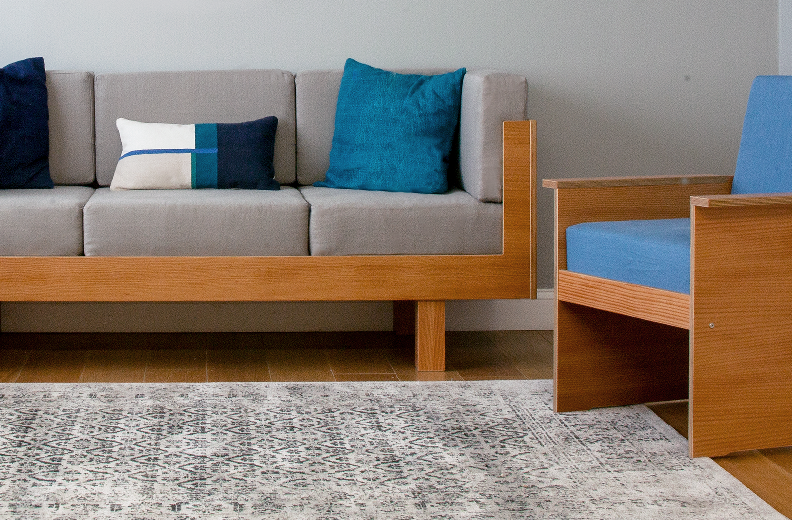 Modern living room with a wooden-framed sofa, grey cushions, blue pillows, and a textured rug.