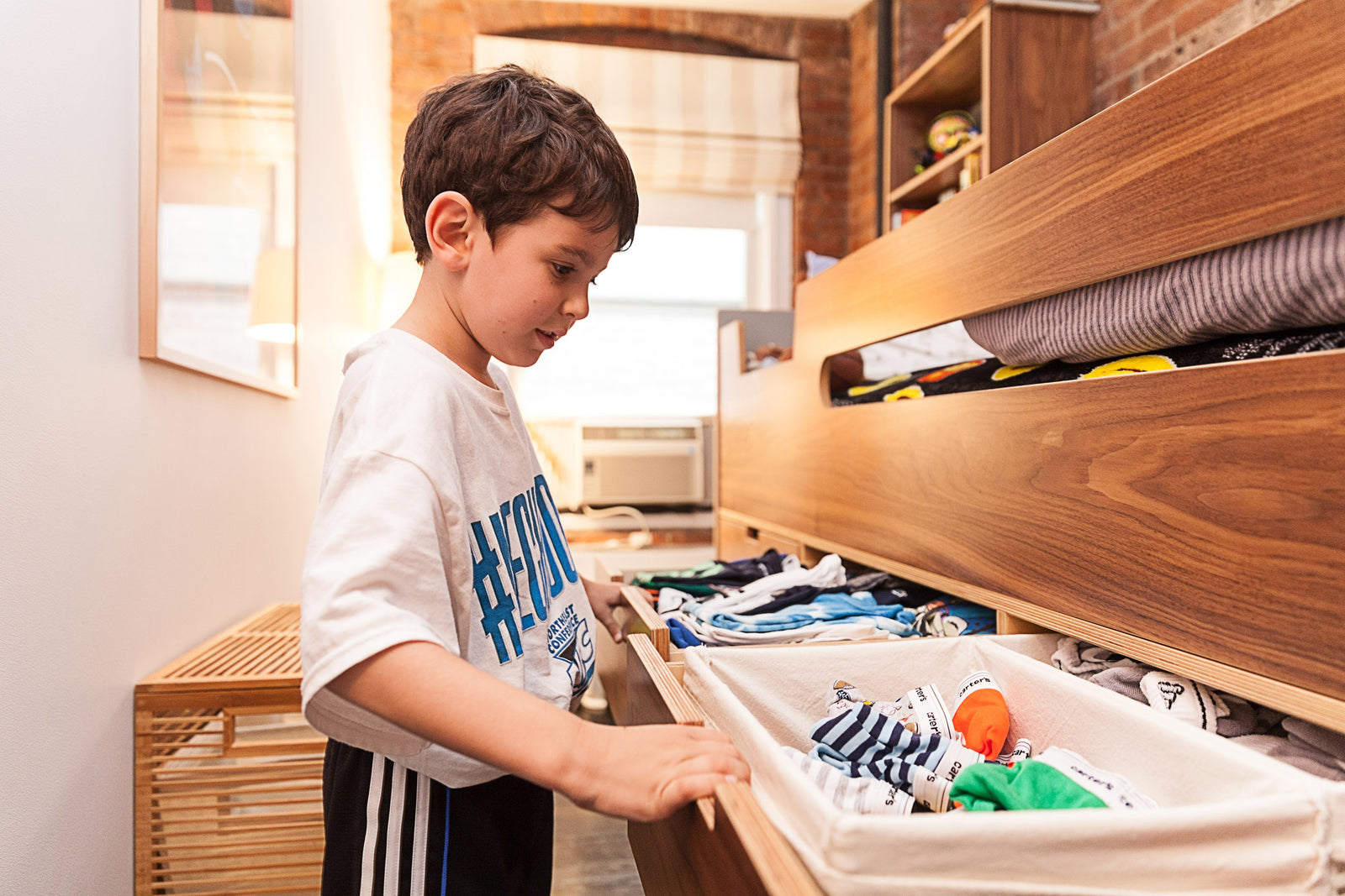 Child with obscured face sorting clothes in a drawer.